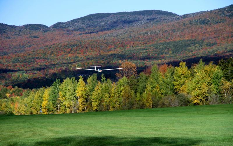 glider landing at airport surrounded by early fall foliage